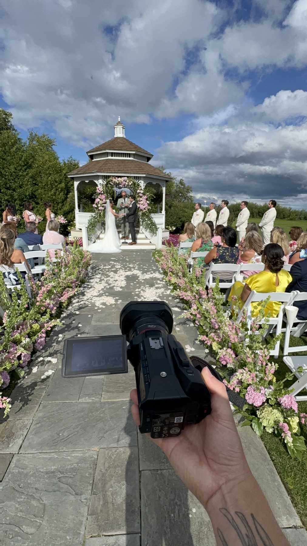 A guest filming an outdoor wedding ceremony